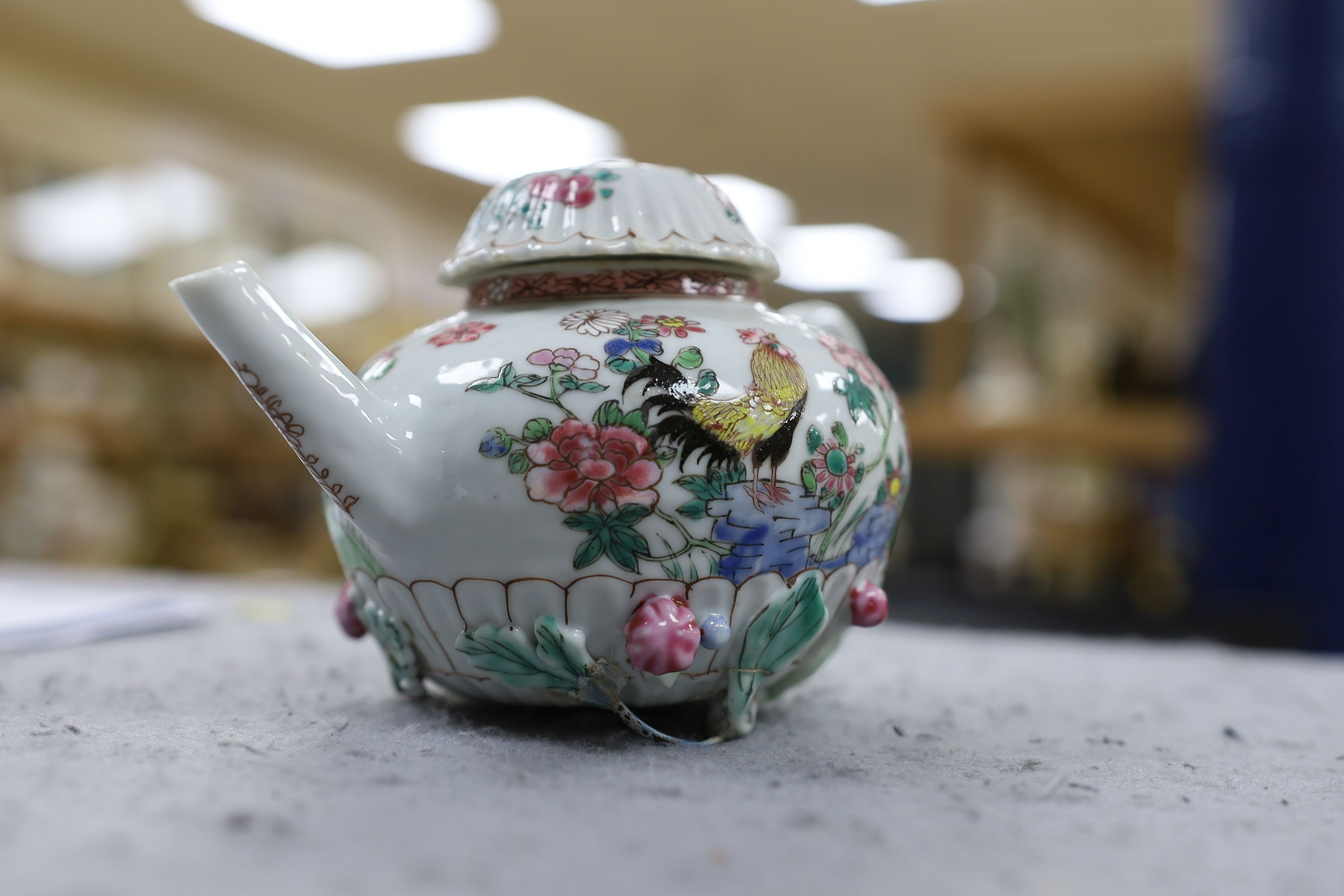 A Chinese famille rose chrysanthemum moulded teapot, early Qianlong period, painted with a cockerel amongst flowers, on a cage work base, 10 cms high